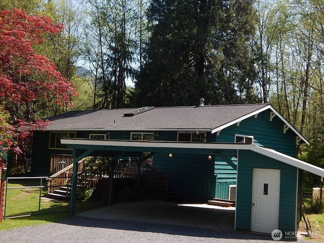 exterior space featuring stairway, fence, a shingled roof, and driveway