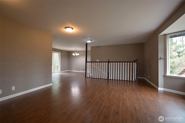 spare room with dark wood finished floors, an inviting chandelier, and baseboards