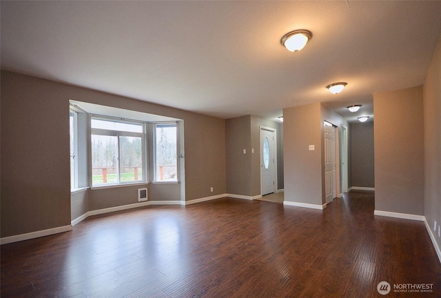 empty room featuring dark wood finished floors, visible vents, and baseboards