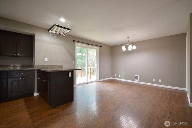 kitchen featuring baseboards, dark wood finished floors, dark stone countertops, a peninsula, and an inviting chandelier