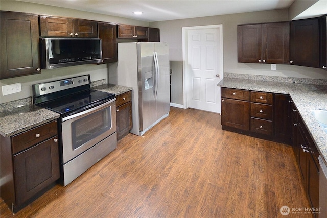 kitchen featuring dark brown cabinets, light stone counters, appliances with stainless steel finishes, and wood finished floors