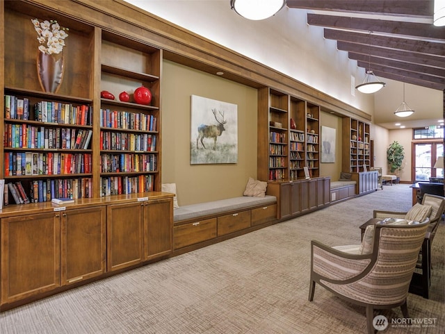 living area with carpet floors, a high ceiling, beamed ceiling, and wall of books