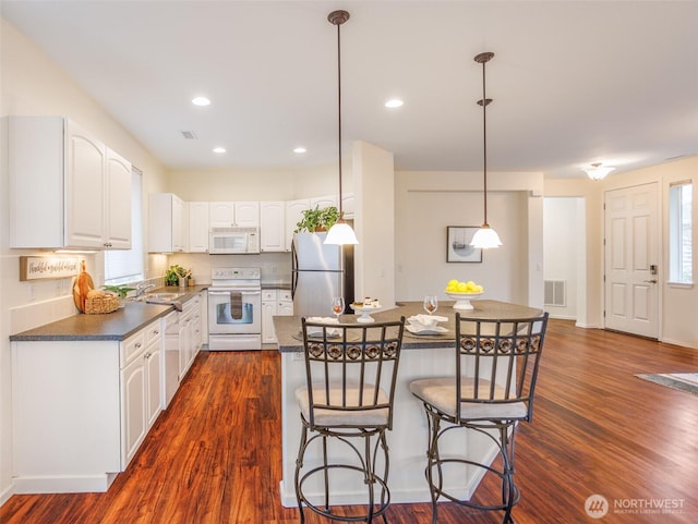 kitchen featuring a breakfast bar area, dark countertops, visible vents, a sink, and white appliances