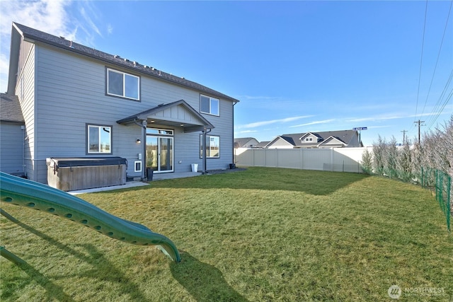 rear view of property featuring a fenced backyard, a lawn, and a hot tub