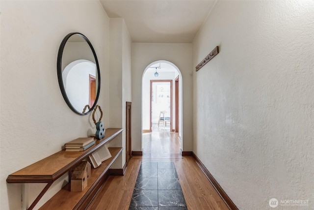 corridor with baseboards, arched walkways, and a textured wall