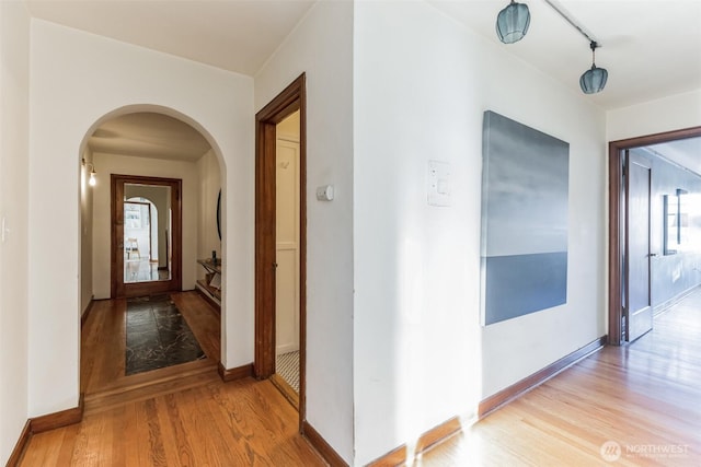 hallway featuring light wood-style floors, baseboards, and arched walkways