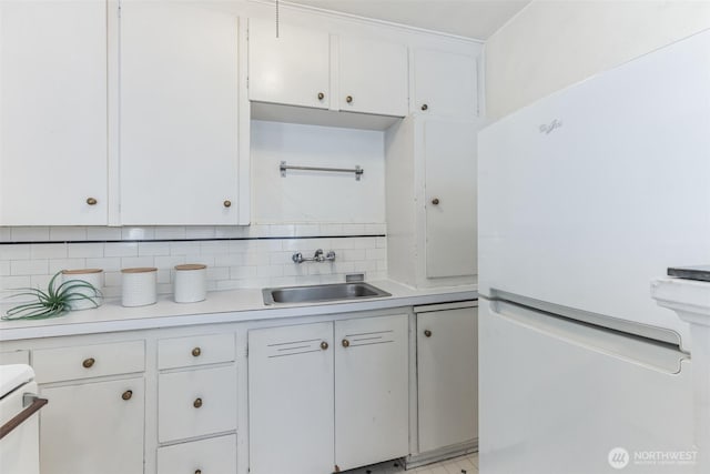 kitchen featuring light countertops, decorative backsplash, freestanding refrigerator, white cabinetry, and a sink