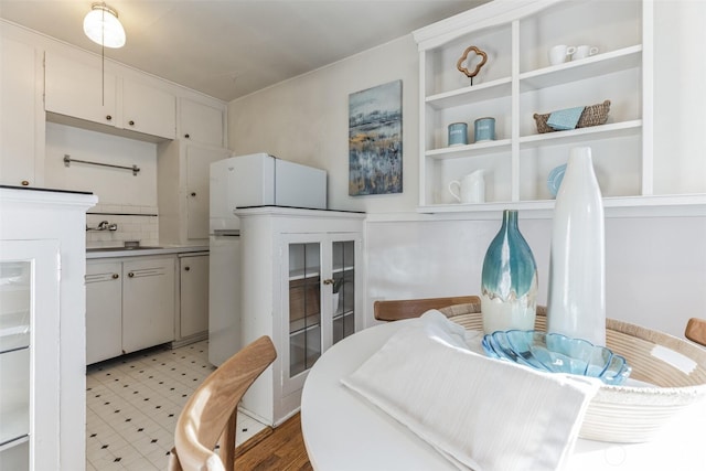 kitchen with a sink, white cabinets, backsplash, freestanding refrigerator, and light floors