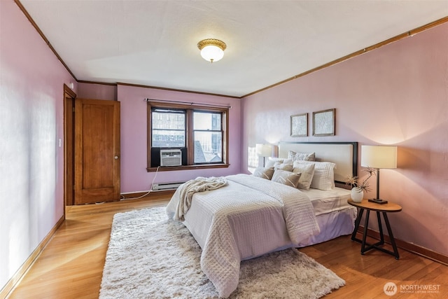 bedroom with cooling unit, a baseboard heating unit, baseboards, light wood-type flooring, and crown molding