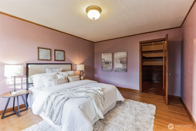 bedroom featuring ornamental molding, a walk in closet, light wood-style floors, and baseboards