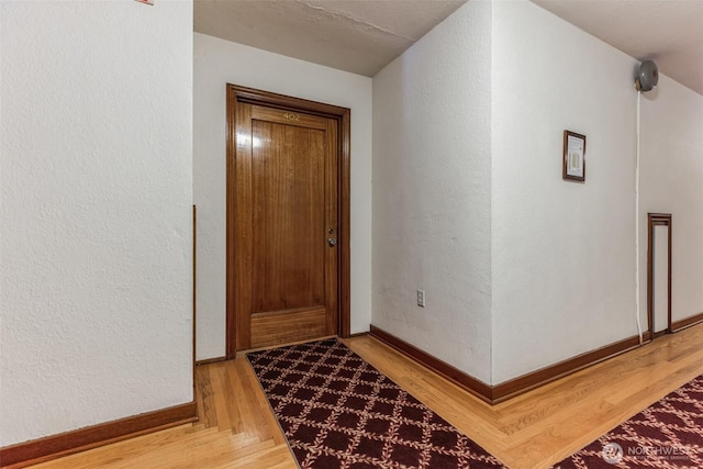 interior space featuring light wood finished floors, baseboards, and a textured wall