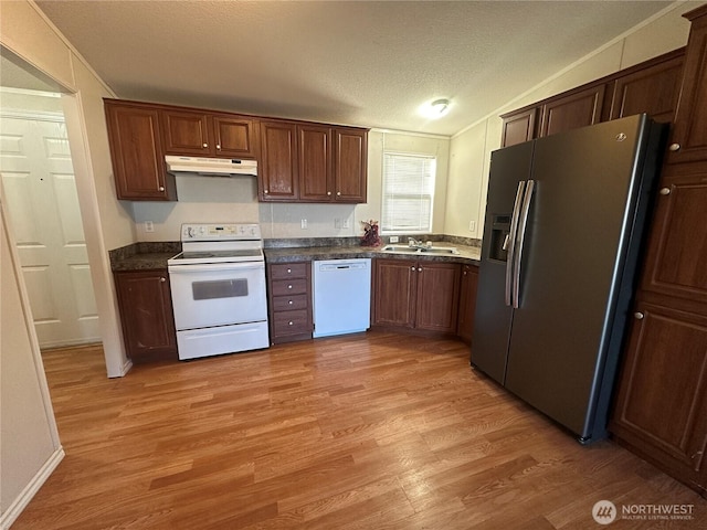 kitchen with under cabinet range hood, white appliances, a sink, light wood-type flooring, and dark countertops