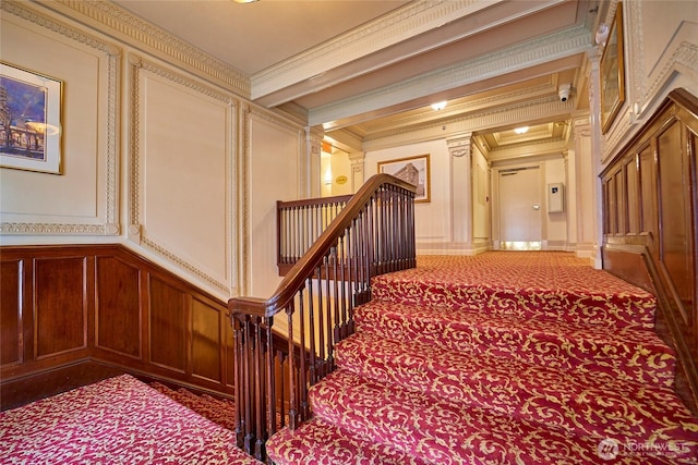 hall with a decorative wall, carpet flooring, an upstairs landing, ornamental molding, and beamed ceiling