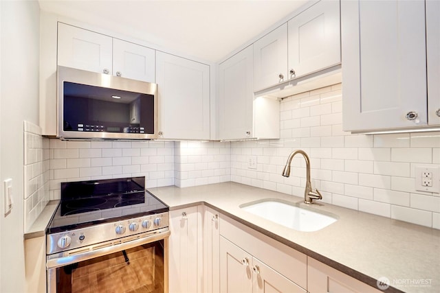 kitchen featuring appliances with stainless steel finishes, a sink, light countertops, white cabinetry, and backsplash