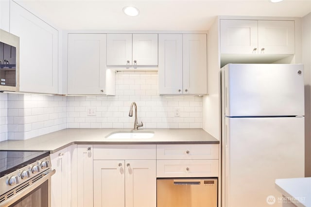 kitchen with appliances with stainless steel finishes, white cabinets, a sink, and backsplash