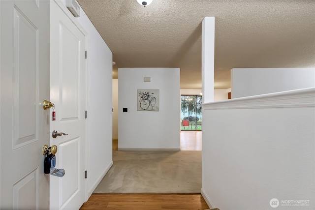 corridor with a textured ceiling, baseboards, and wood finished floors