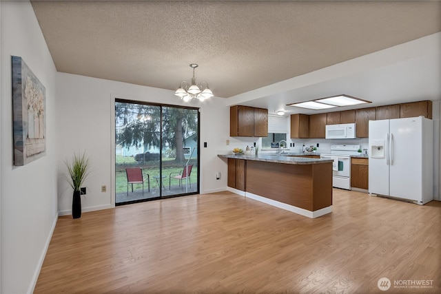 kitchen featuring white appliances, light wood finished floors, a peninsula, a textured ceiling, and a notable chandelier