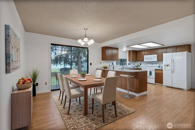 dining room with a textured ceiling, light wood-type flooring, and an inviting chandelier