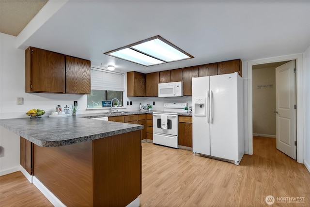 kitchen featuring white appliances, dark countertops, light wood-style flooring, a peninsula, and a sink