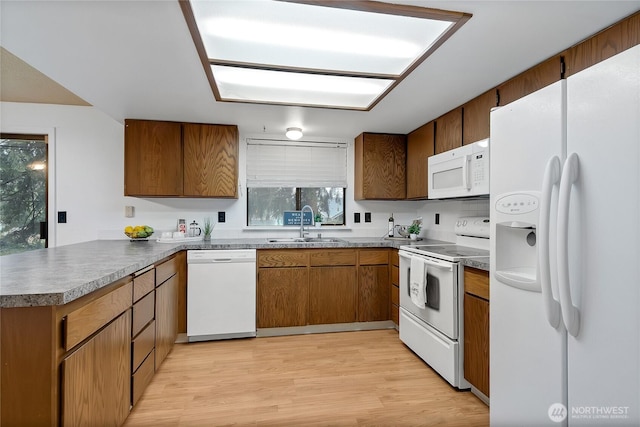 kitchen featuring white appliances, light wood finished floors, brown cabinets, a peninsula, and a sink