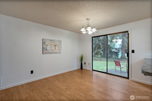 empty room featuring a textured ceiling, light wood-type flooring, baseboards, and an inviting chandelier