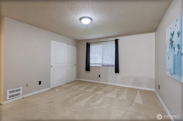 unfurnished room with light carpet, visible vents, baseboards, and a textured ceiling