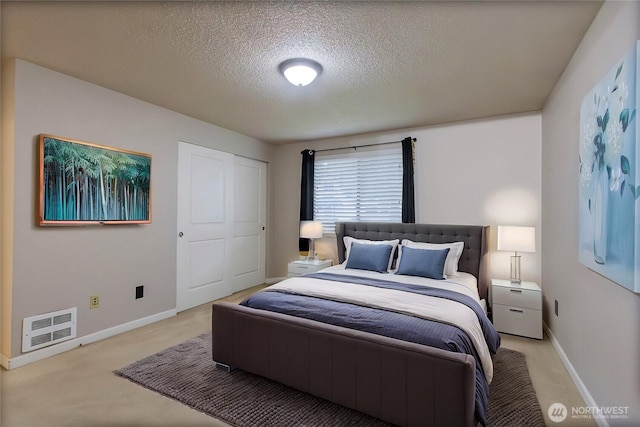 bedroom with heating unit, baseboards, a textured ceiling, and light colored carpet