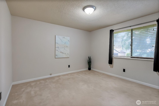 spare room with baseboards, a textured ceiling, and light colored carpet