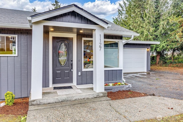 property entrance with a shingled roof, board and batten siding, a garage, and aphalt driveway