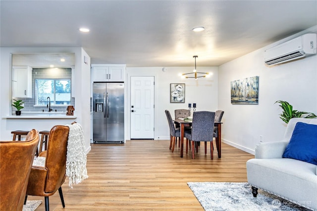 dining room with a wall unit AC, a notable chandelier, light wood-style flooring, and baseboards