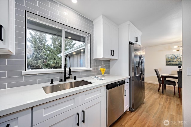 kitchen featuring stainless steel appliances, a sink, light countertops, light wood-type flooring, and backsplash