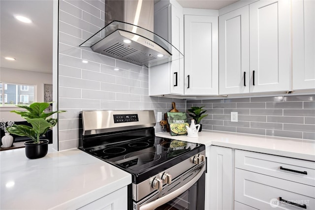 kitchen with tasteful backsplash, wall chimney exhaust hood, stainless steel electric range oven, and light countertops