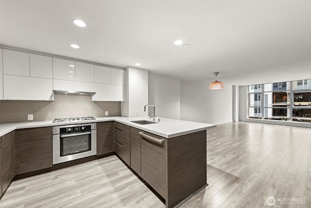 kitchen featuring modern cabinets, stainless steel appliances, light countertops, light wood-type flooring, and a sink