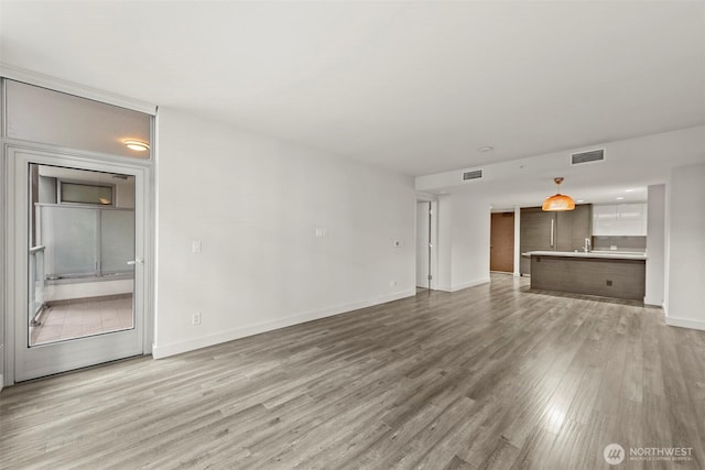 unfurnished living room with light wood-style flooring, visible vents, and baseboards