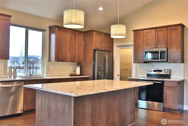 kitchen featuring a sink, light stone counters, a kitchen island, stainless steel appliances, and vaulted ceiling