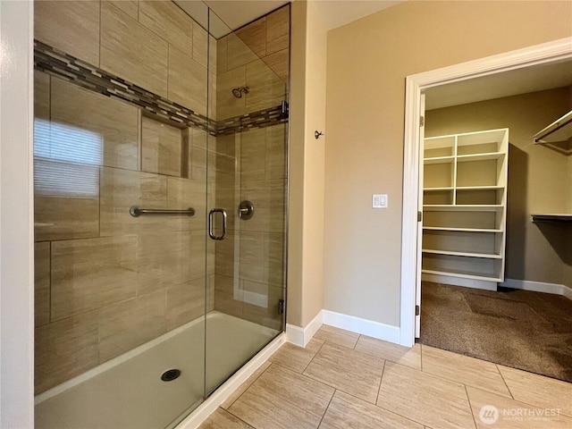 full bathroom featuring a shower stall, a spacious closet, and baseboards