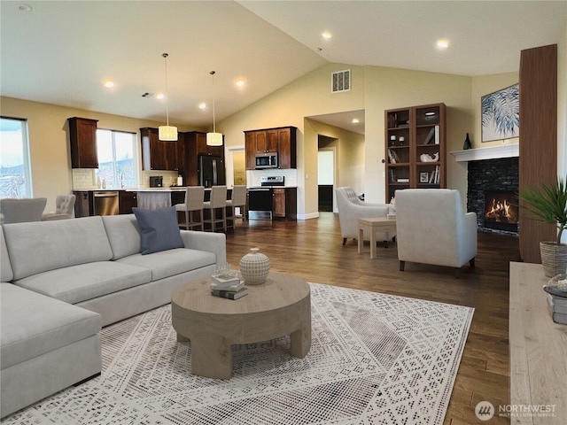 living room with visible vents, lofted ceiling, recessed lighting, dark wood-style flooring, and a lit fireplace