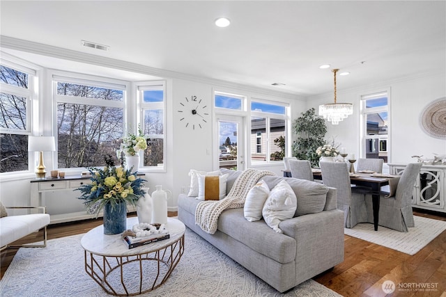 living area featuring an inviting chandelier, wood finished floors, visible vents, and crown molding