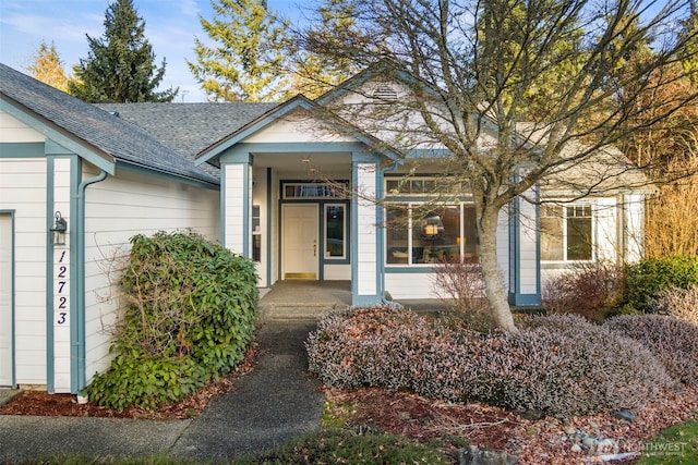 view of exterior entry with an attached garage and roof with shingles