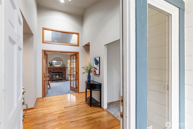 entryway with a brick fireplace, a high ceiling, baseboards, and light wood finished floors