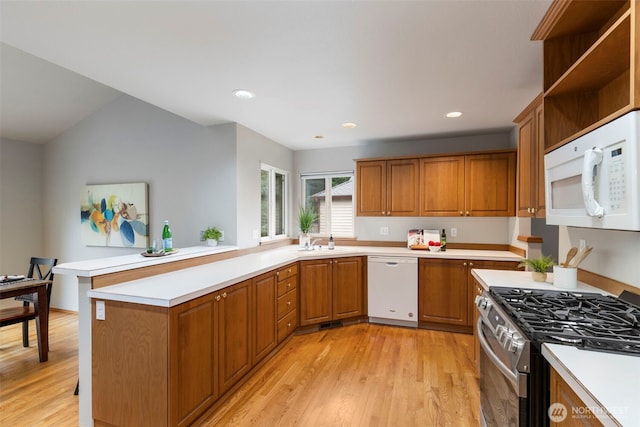 kitchen with brown cabinets, light countertops, light wood-style flooring, a sink, and white appliances