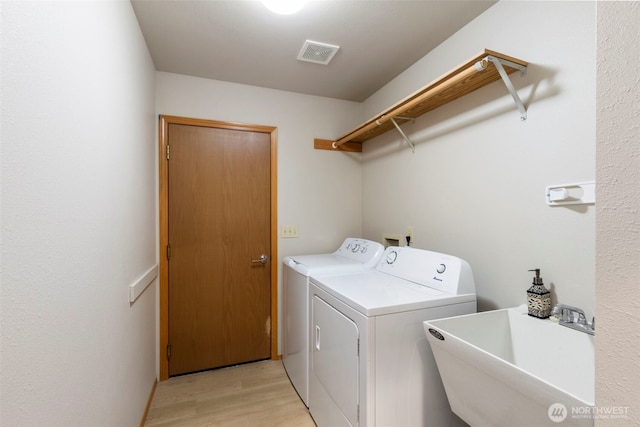 laundry area with laundry area, separate washer and dryer, a sink, visible vents, and light wood-style floors