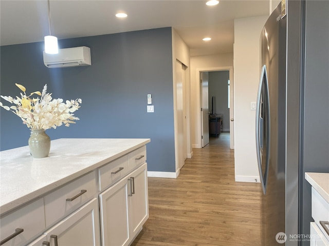 3601 Page St, Port Angeles, WA 98362 - kitchen with freestanding refrigerator, a wall unit AC, light wood-style flooring, white cabinets, and decorative light fixtures