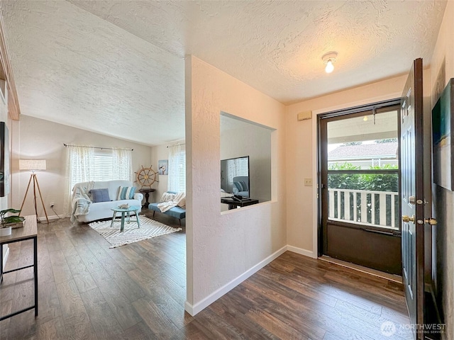 entryway featuring baseboards, a textured wall, dark wood-type flooring, vaulted ceiling, and a textured ceiling