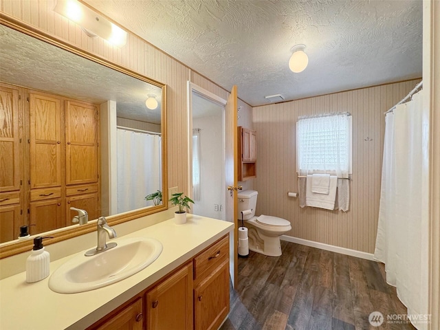 bathroom featuring baseboards, toilet, wood finished floors, a textured ceiling, and vanity