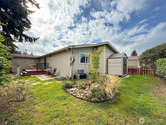 rear view of property with a storage shed, a yard, an outbuilding, and fence