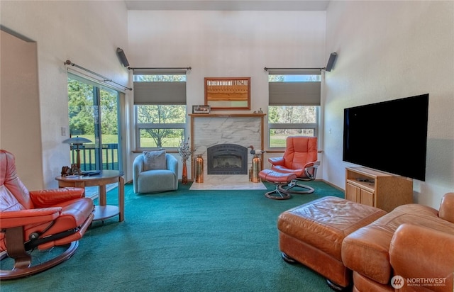 living area with a stone fireplace, carpet flooring, a towering ceiling, and a healthy amount of sunlight