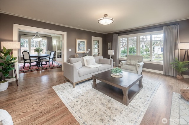 living room featuring a healthy amount of sunlight, crown molding, baseboards, and wood finished floors