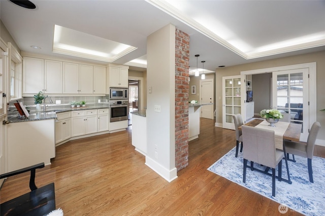 dining room featuring light wood-type flooring, a raised ceiling, and baseboards