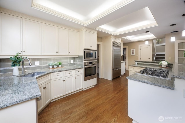 kitchen with a raised ceiling, a sink, and built in appliances